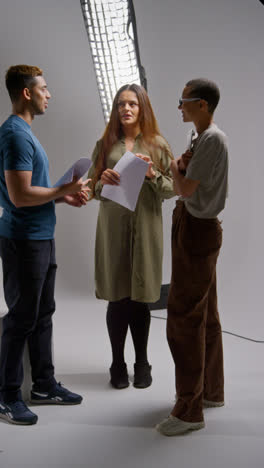 Vertical-Video-Of-Film-Director-Talking-With-Male-And-Female-Actors-Holding-Scripts-Rehearsing-For-Shooting-Movie-Or-Video-In-Studio-1